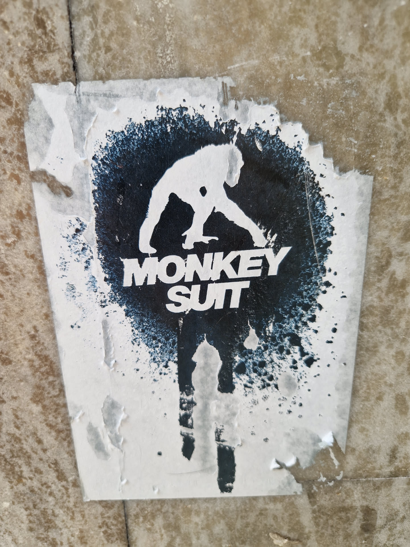A worn sticker featuring a stylized monkey silhouette in a dark ink splatter design. The text 'MONKEY SUIT' is visible beneath the monkey.