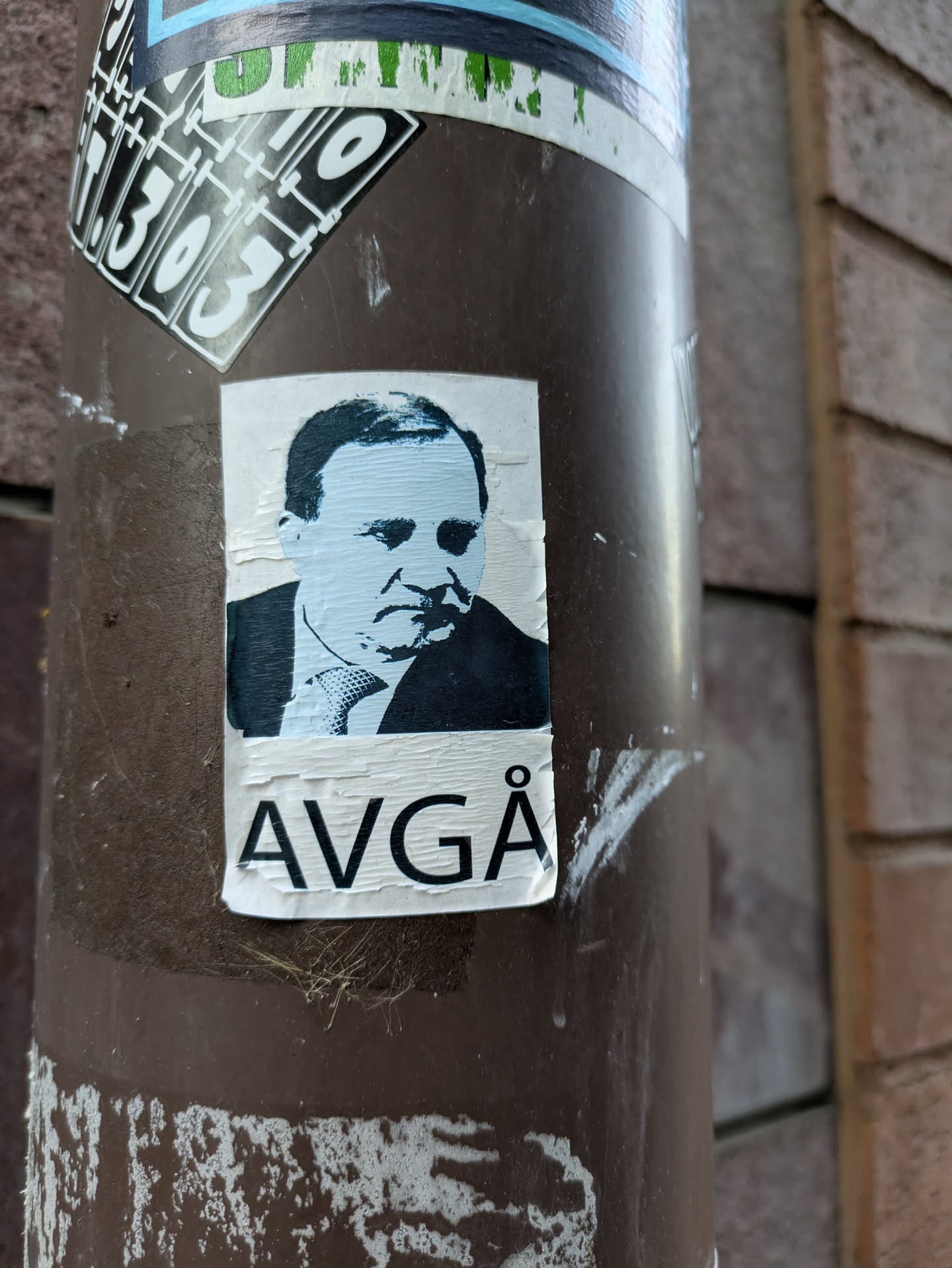 A sticker featuring a stylized black and white portrait of a man with the word "AVGÅ" written below.  The word likely means "resign" in Swedish.