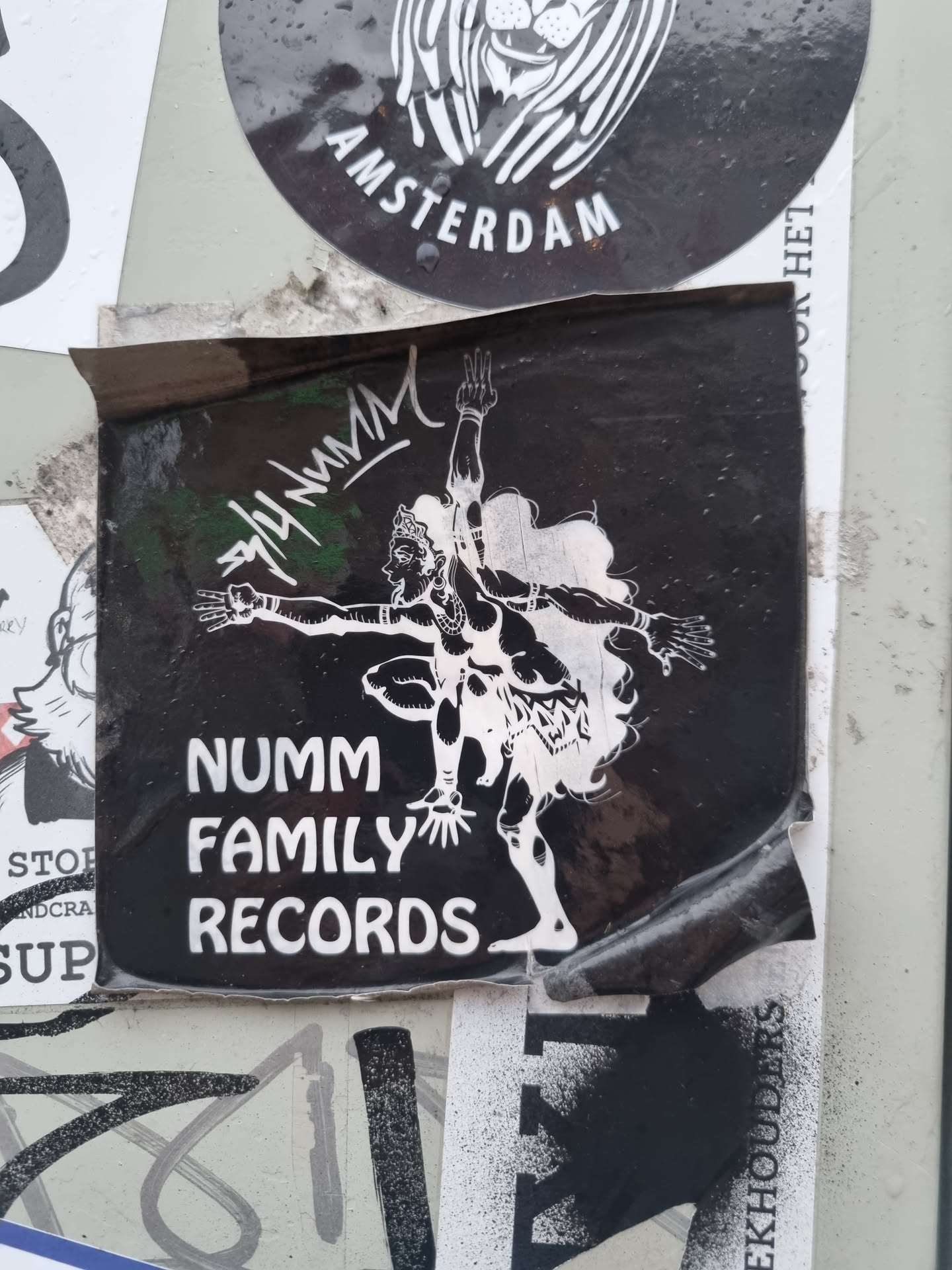 A black and white sticker featuring the logo for Numm Family Records. The logo includes a stylized figure in a dancing pose. The sticker is slightly damaged around the edges.