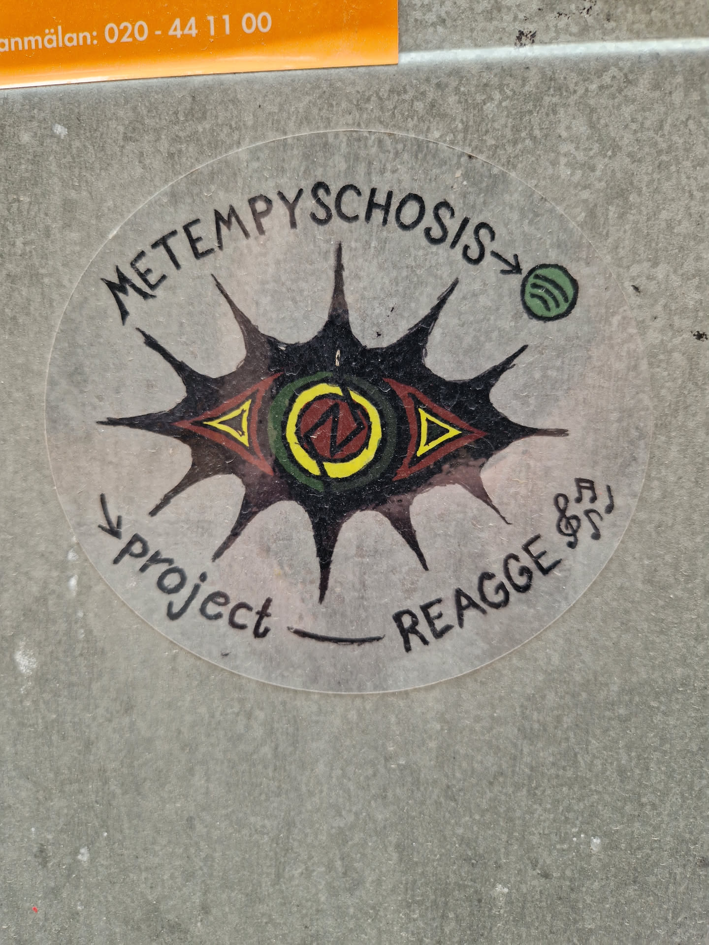 Round sticker featuring an eye with sun rays and the text 'METEMPYSCHOSIS' and 'project _ REAGGE'. A Spotify logo is present on the right side. 