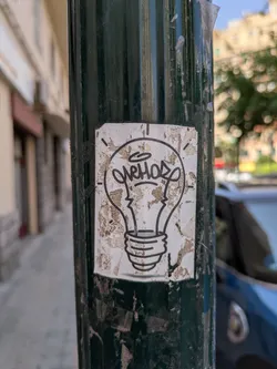 This is a sticker of a simple line art drawing of a light bulb. The sticker has some scratches and tears, and some dirt spots.