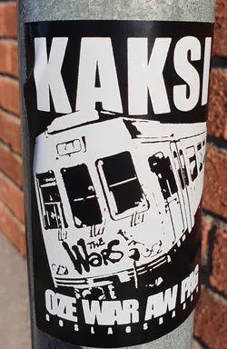 Black and white sticker featuring a train with graffiti that says "The Wars" and the text "KAKSI OZE WAR AW POG" at the top and bottom. The sticker has a punk aesthetic.