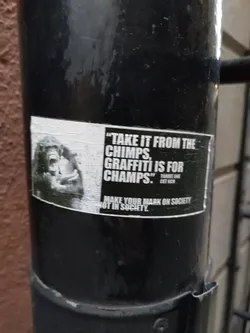 A black and white sticker featuring a chimpanzee and a quote about graffiti. The sticker promotes making a mark on society through graffiti.