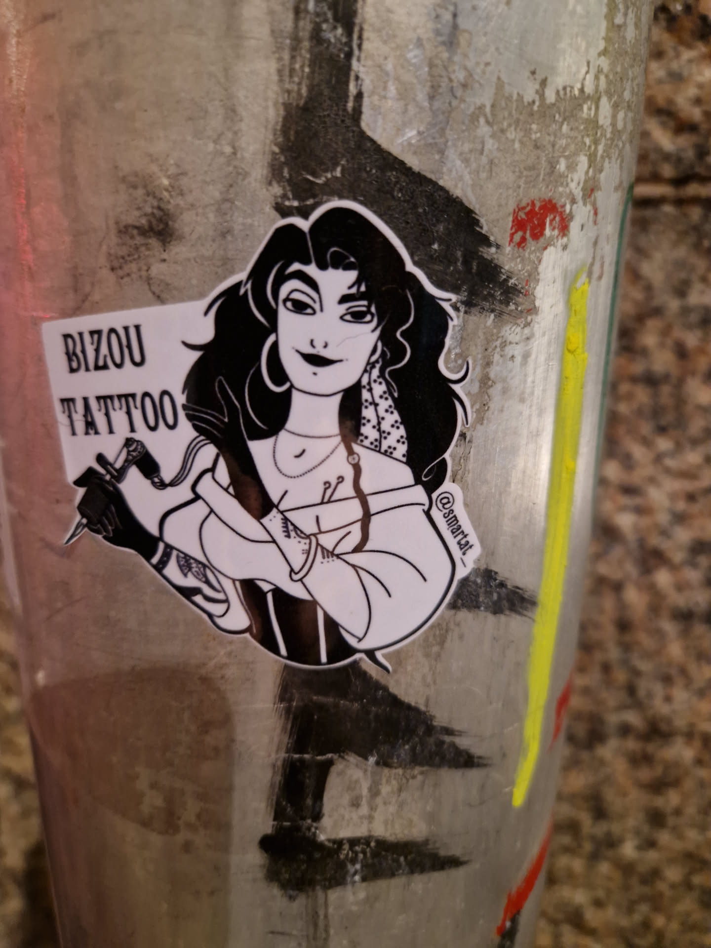 A sticker featuring a black and white illustration of a woman with long dark hair, holding a tattoo machine. The text 'Bizou Tattoo' is written at the top of the sticker. The artist's Instagram handle is visible at the bottom right corner.
