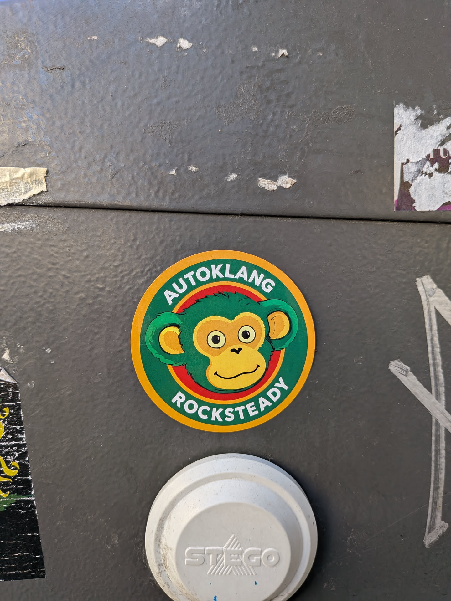 A circular sticker with a thick yellow border. Inside is a dark green band containing the bold white text 'AUTOKLANG' curved along the top and 'ROCKSTEADY' curved along the bottom. The center features a stylized cartoon monkey head with green fur, yellow facial skin and inner ears, large wide-open eyes, and a slight smirk, outlined by a red circle.