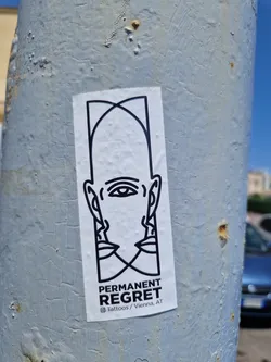 Black and white sticker with a graphic design of a face and the words "Permanent Regret" underneath.  The sticker is affixed to a grey metal pole. The text also includes @Tattoos / Vienna AT