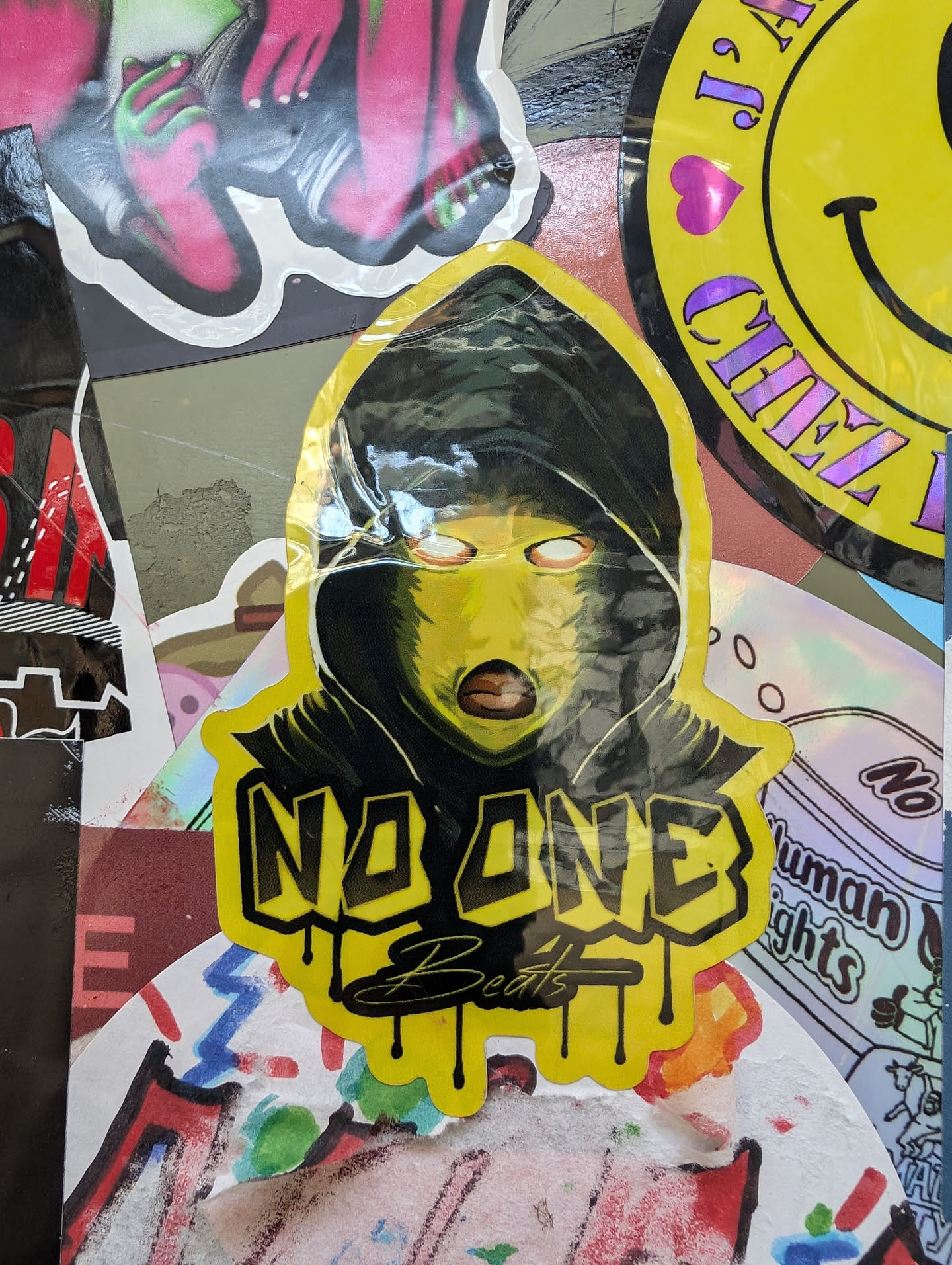 Yellow sticker with a stylized illustration of a person wearing a black balaclava and a yellow mask. The text 'NO ONE Beats' is prominently displayed with a dripping effect.
