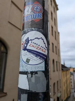 The sticker is circular with a white background. At the top left, it features a stylized fleur-de-lis in dark blue. The text "VIOLA CLUB" is written in dark blue uppercase letters, and "LUCERNA" is written below it in bold red uppercase letters. Below the text, there is a depiction of a pier or bridge with railings, rendered in dark blue lines against a white background, with a blue mountain range in the distance. A small QR code is positioned on the left side of the pier. The year "2024" is written in small red text to the right of the pier. A thin blue border encircles the sticker. The bottom of the sticker has some blue and white distressed elements and text which is partially obscured.