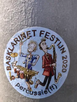 Round sticker featuring an illustration of two cartoon musicians; one playing the xylophone and the other a bass clarinet. The text around the illustration says "Bassklarinet Festijn 2020" and  "percussie (f)" at the bottom. 