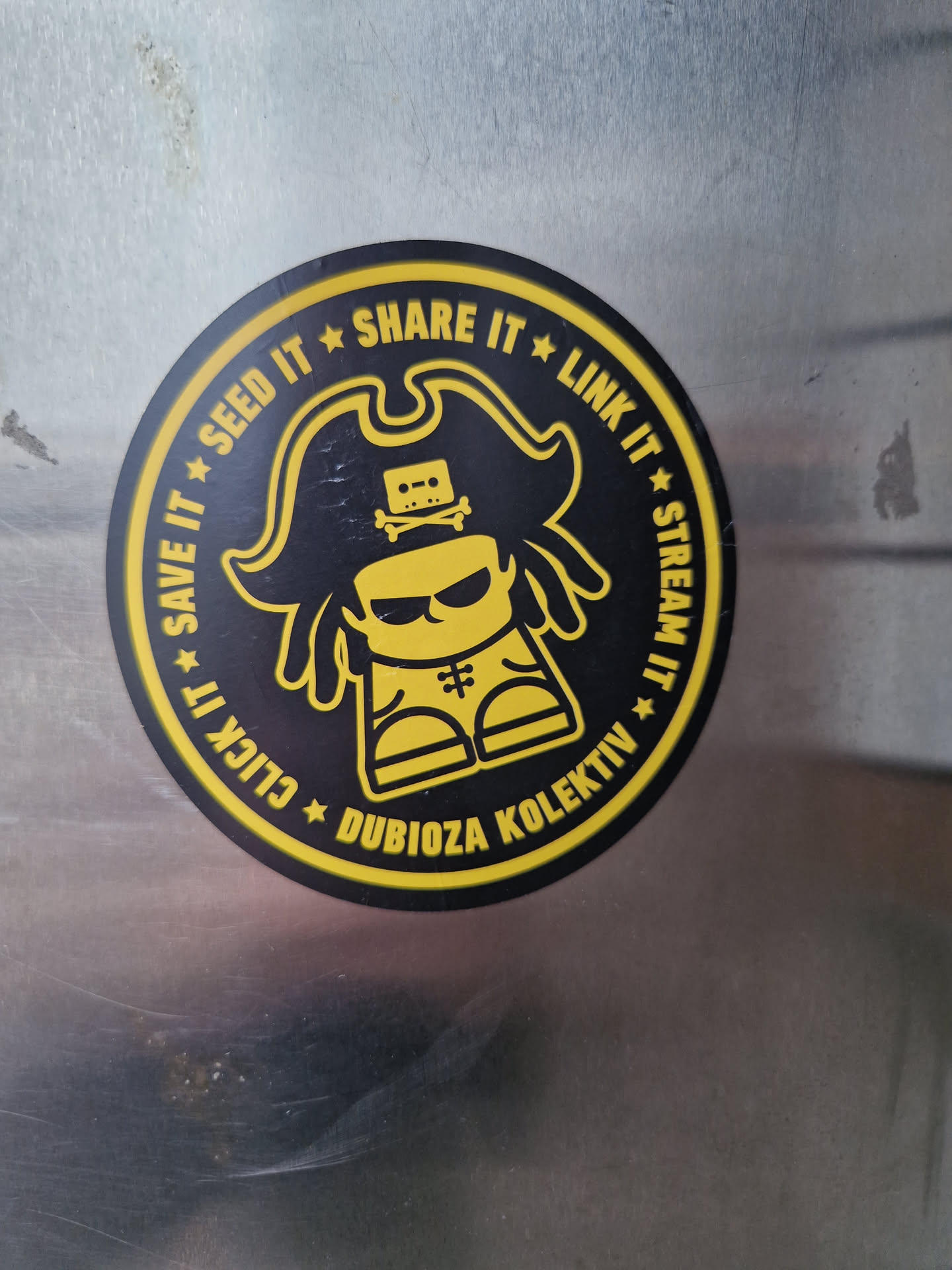 Round sticker featuring a cartoon pirate with a cassette tape on his head. The text around the character says:  Seed it, Share it, Link it, Stream it, Save it, Click it.  The name Dubioza Kolektiv is at the bottom.