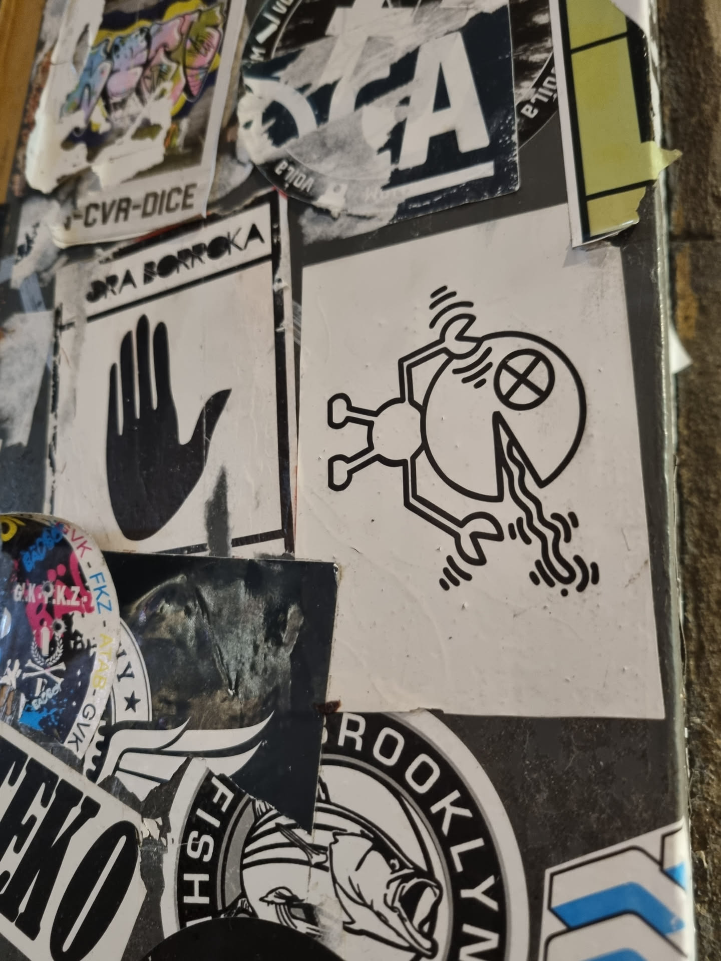 Close-up of a sticker featuring a simple, graphic design. The sticker is black and white and depicts a small figure that appears to be holding or interacting with a slice of pizza. The style is minimalistic and geometric.
