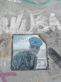 A sticker featuring a man wearing goggles and a hat.  The sticker includes a QR code and a SoundCloud link.