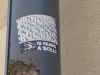 A sticker on a grey pipe with the text "Bring da motherfuckin ruckus" and a picture of a shoe. At the bottom it says "12 years a solli"