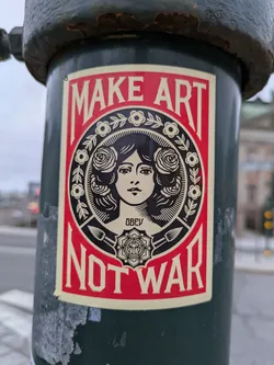 A sticker featuring a woman's face surrounded by roses and the text 'MAKE ART NOT WAR'. The sticker is predominantly red and beige, and the woman's face is styled in a vintage woodcut fashion. The OBEY logo is visible in the bottom center.