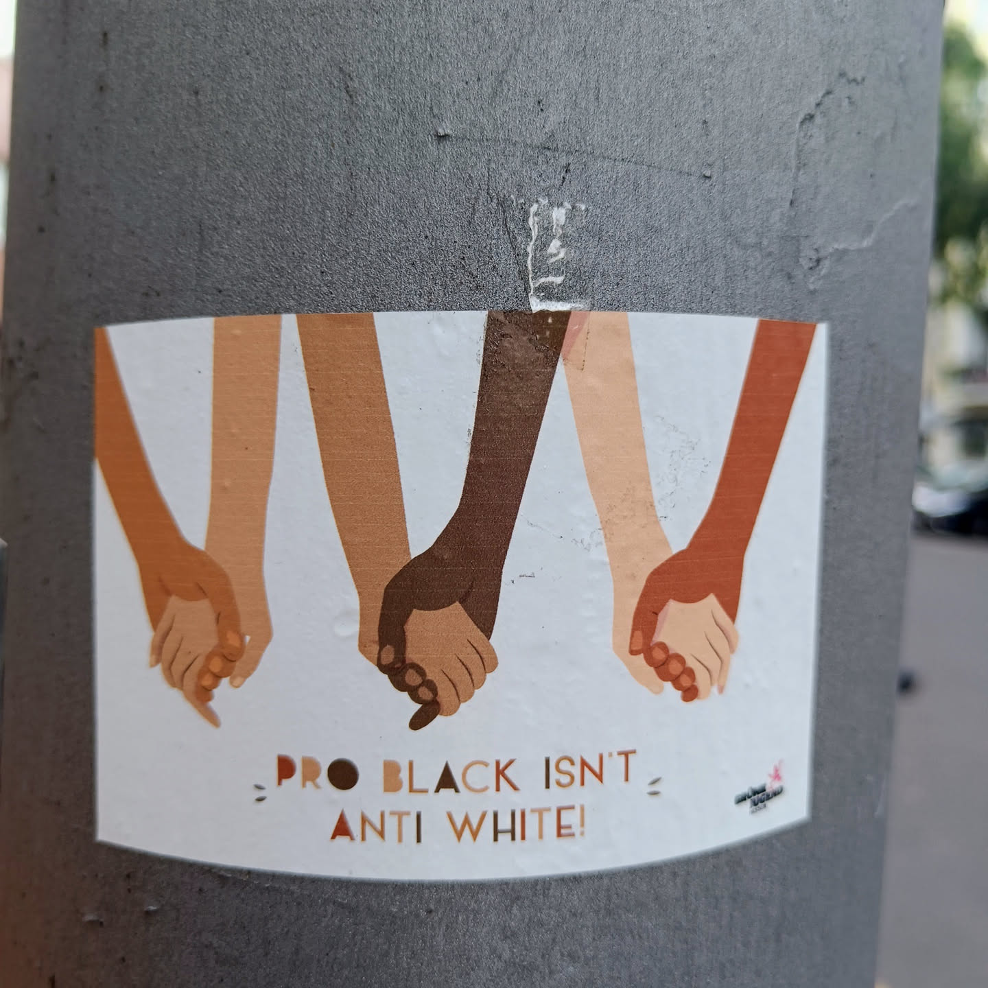 Sticker with an illustration of four pairs of hands holding each other, representing different skin tones.  The text on the sticker states "Pro Black Isn't = Anti White!"