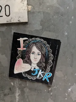 A sticker featuring a drawing of a woman with the initials JKR and a heart. The text 'The Famous Artist Birdy Rose' is written on the side. 