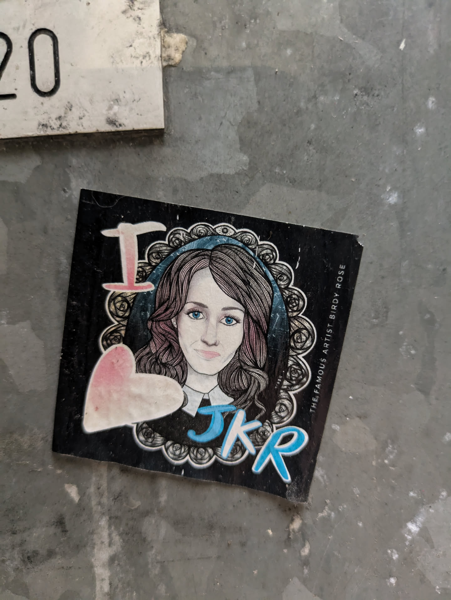 A sticker featuring a drawing of a woman with the initials JKR and a heart. The text 'The Famous Artist Birdy Rose' is written on the side. 