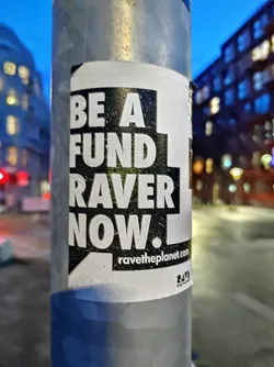 A sticker on a pole with the text 'Be a fund raver now.' and the website ravetheplanet.com.  The sticker uses bold, black text on a white background with a speech bubble design. 