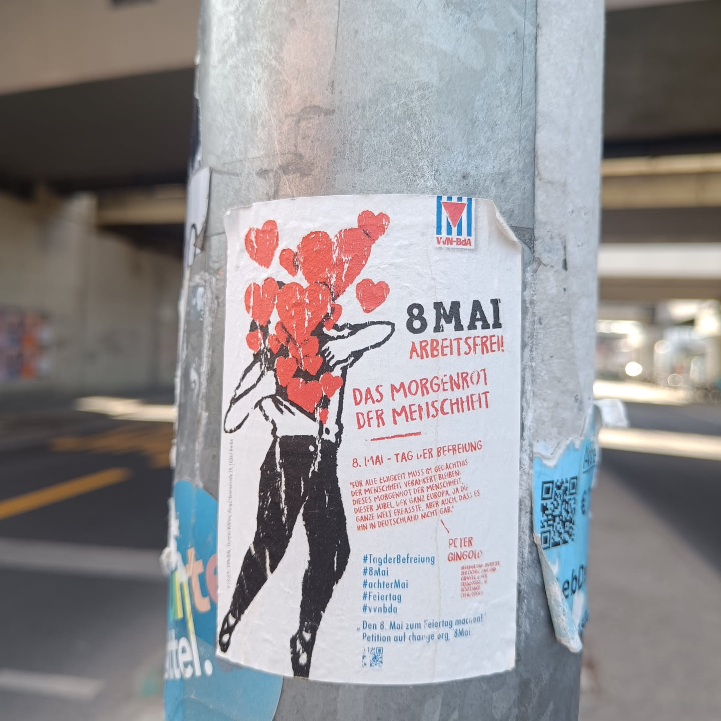 Sticker advocating for May 8th as a public holiday, possibly in Germany, featuring an illustration of a person holding hearts.  The text includes hashtags and mentions a petition.