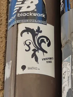 A sticker with a black and white design. It features a stylized floral motif with drips, and the text "FRIENDLY FIRE" and a website address. 
