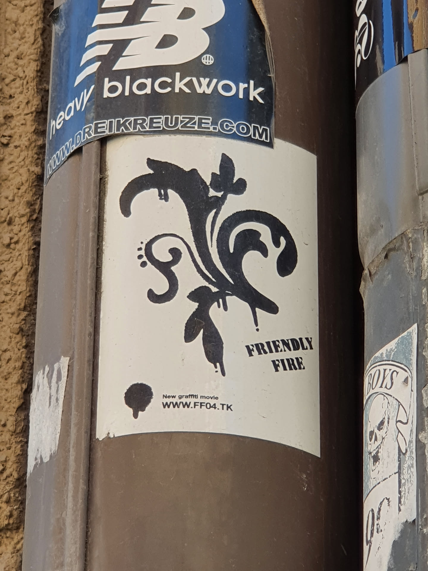 A sticker with a black and white design. It features a stylized floral motif with drips, and the text "FRIENDLY FIRE" and a website address. 