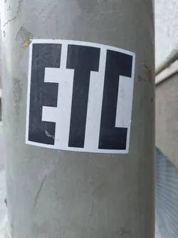 A simple sticker with the letters ETC in black on a white background. The sticker is attached to a grey pole.