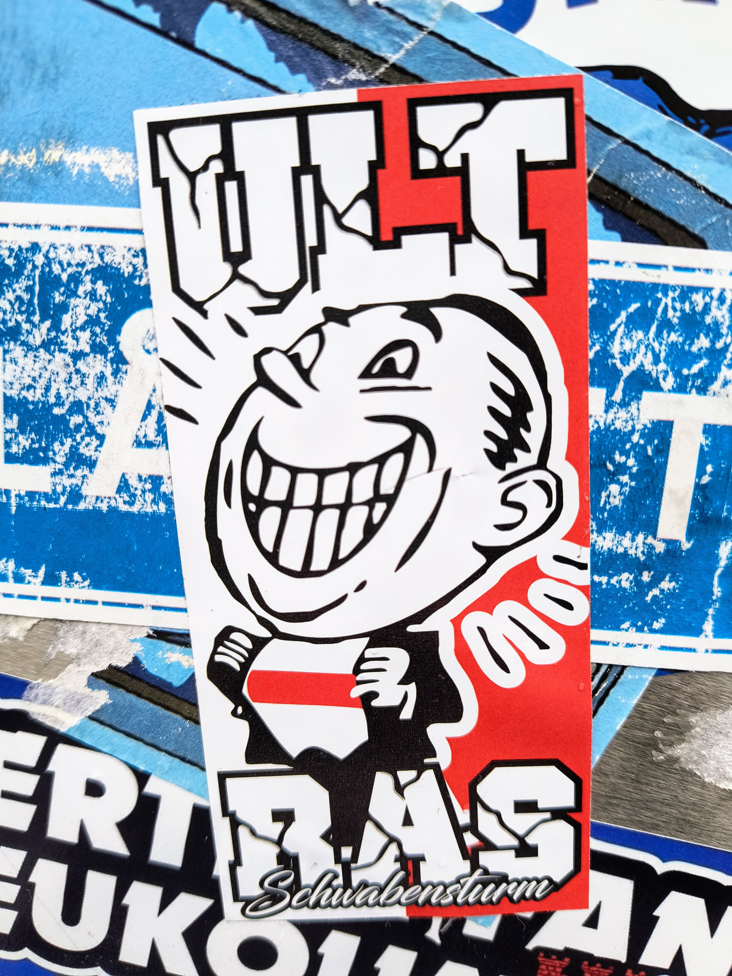 A sticker featuring a cartoon face with a wide smile and the text "ULT RAS" in bold letters. The colors are predominantly black, red, and white.  There is smaller text at the bottom that reads "Schwabensturm".