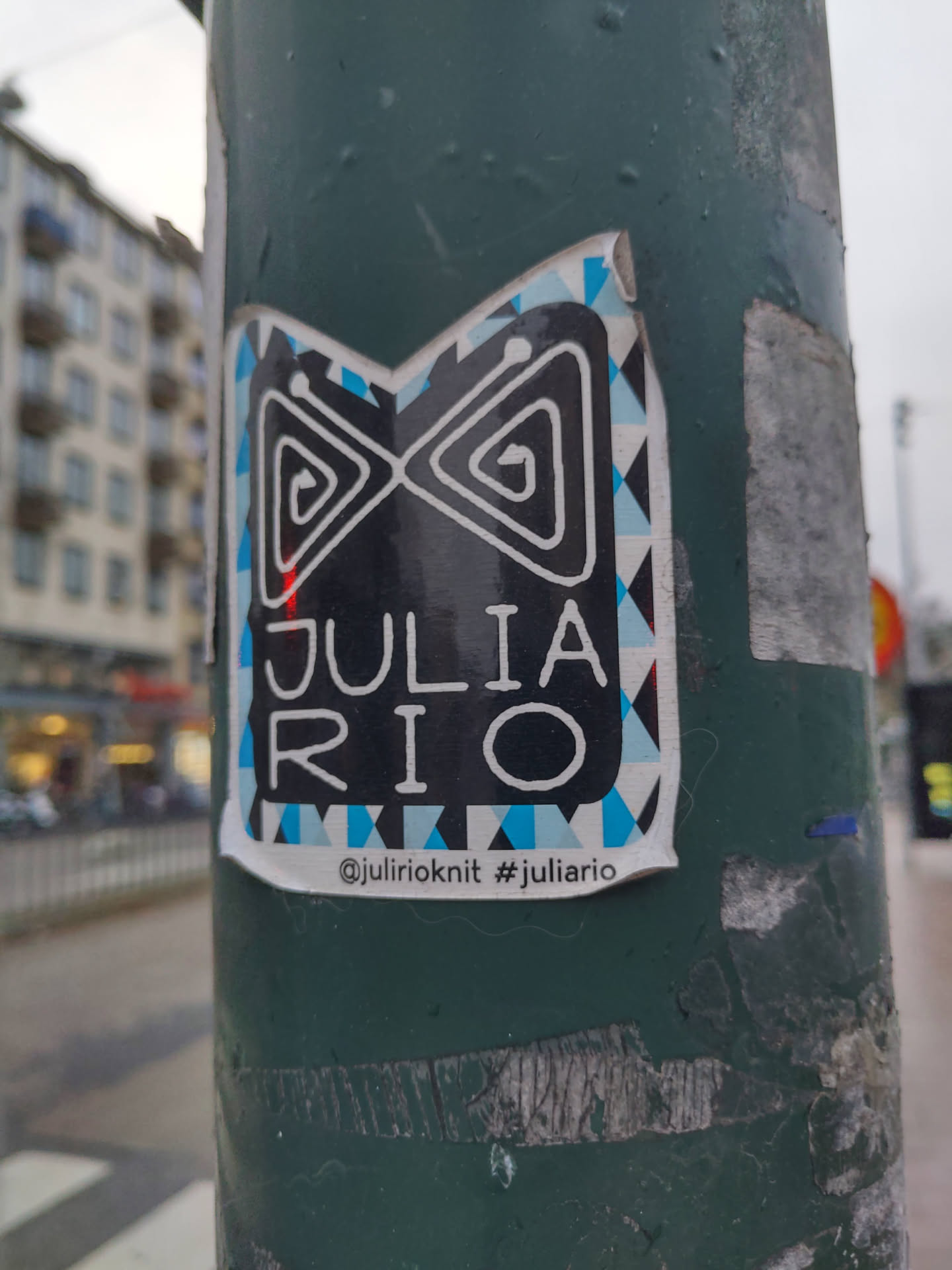 A sticker with a black and white design and blue accents. It has the name "Julia Rio" written in the center. The bottom of the sticker shows a social media handle and a hashtag.