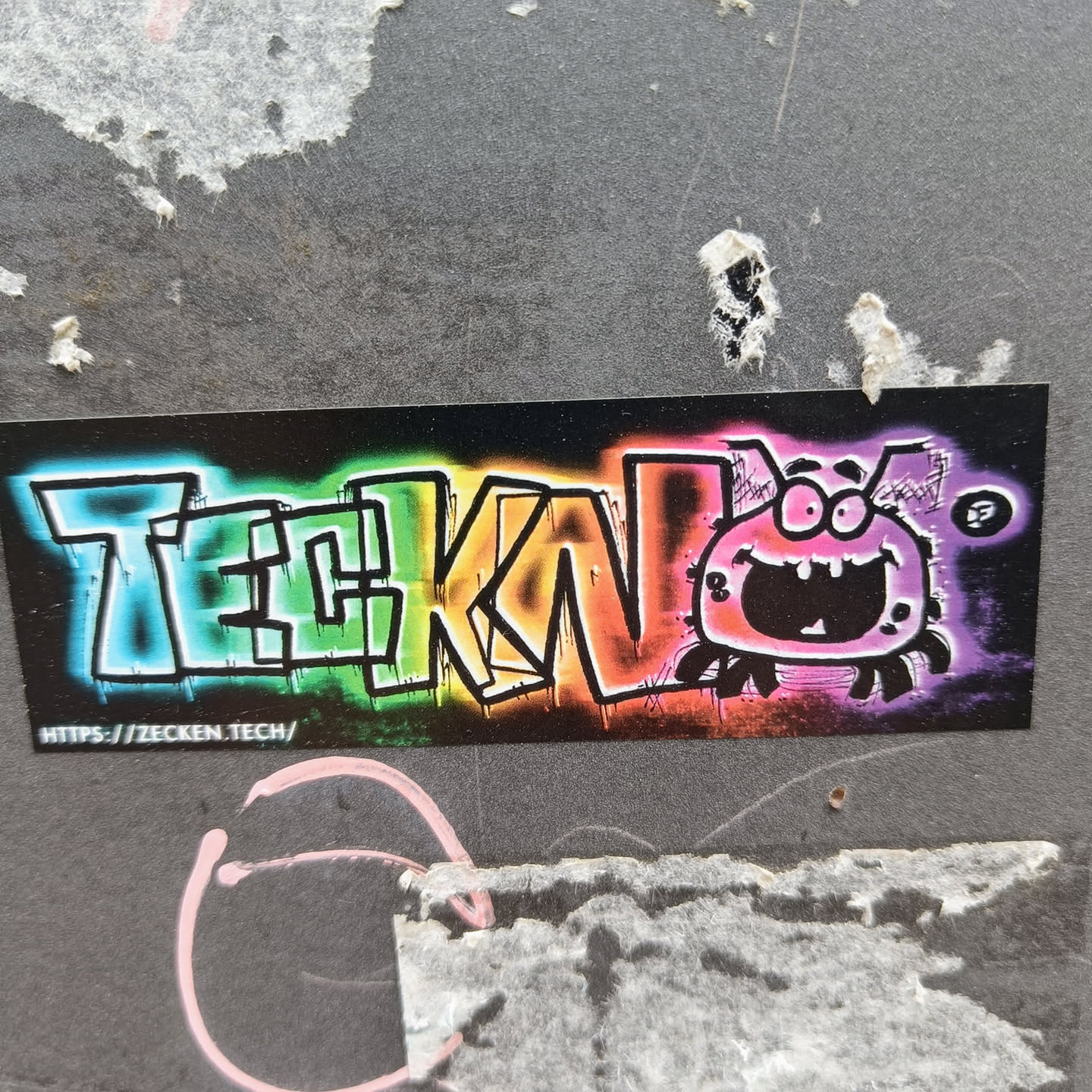 A vibrant sticker featuring the word "TEKNO" in graffiti style with a rainbow color scheme. A cartoonish bug with a large grin is positioned to the right of the text. The sticker has a black background and includes a URL at the bottom.