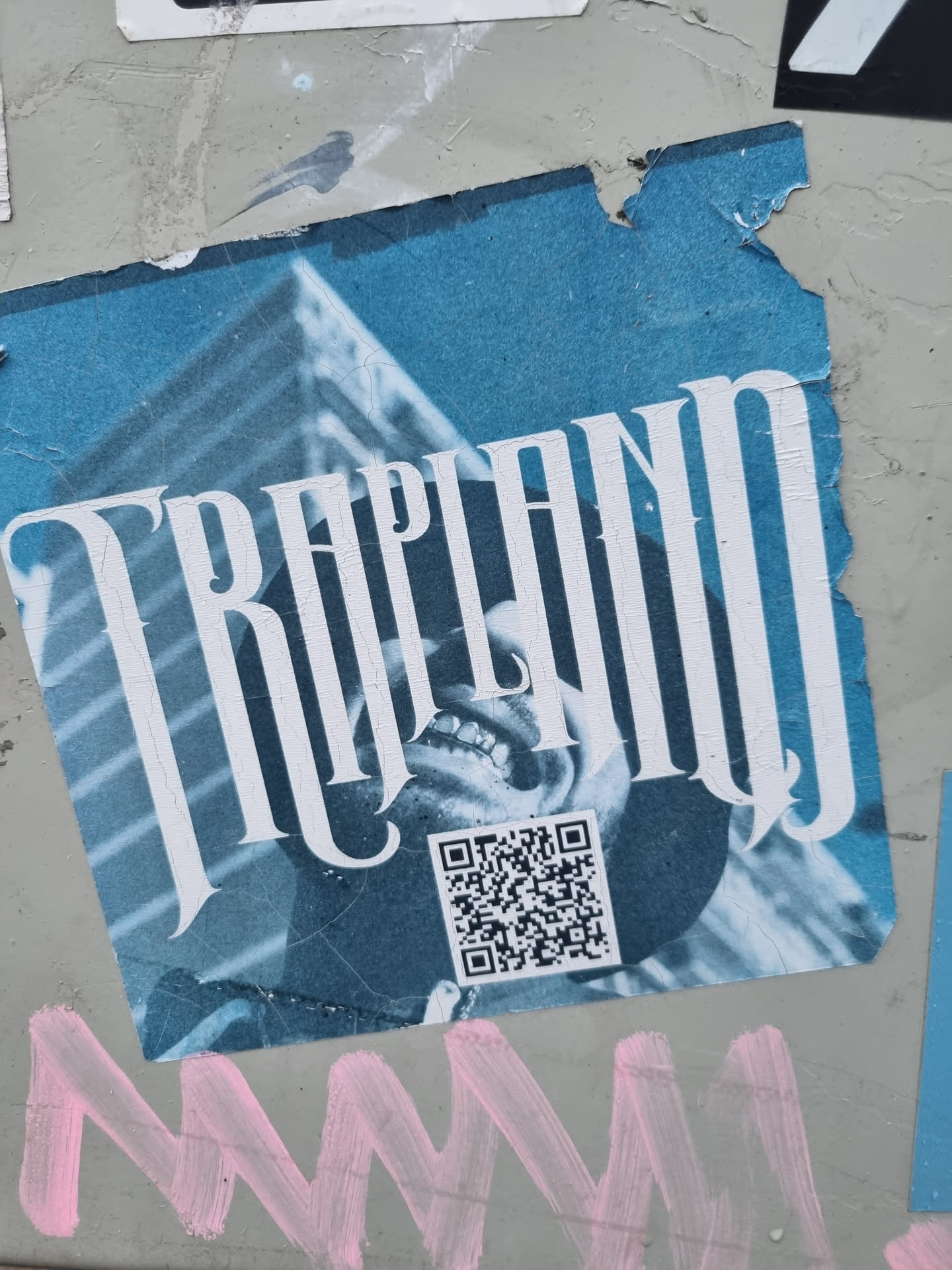 A blue and white sticker with the word "TRAPLAND" in a stylized font.  It features an image of a person's face and a QR code. The sticker shows some signs of wear and tear.