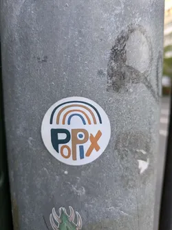 This sticker is on a gray pole. The sticker has a semi-circle rainbow at the top, with arcs of brown, beige and dark blue. Below the rainbow, the sticker reads "PPlx" with the "PP" in dark blue, "l" in beige and "x" in brown.