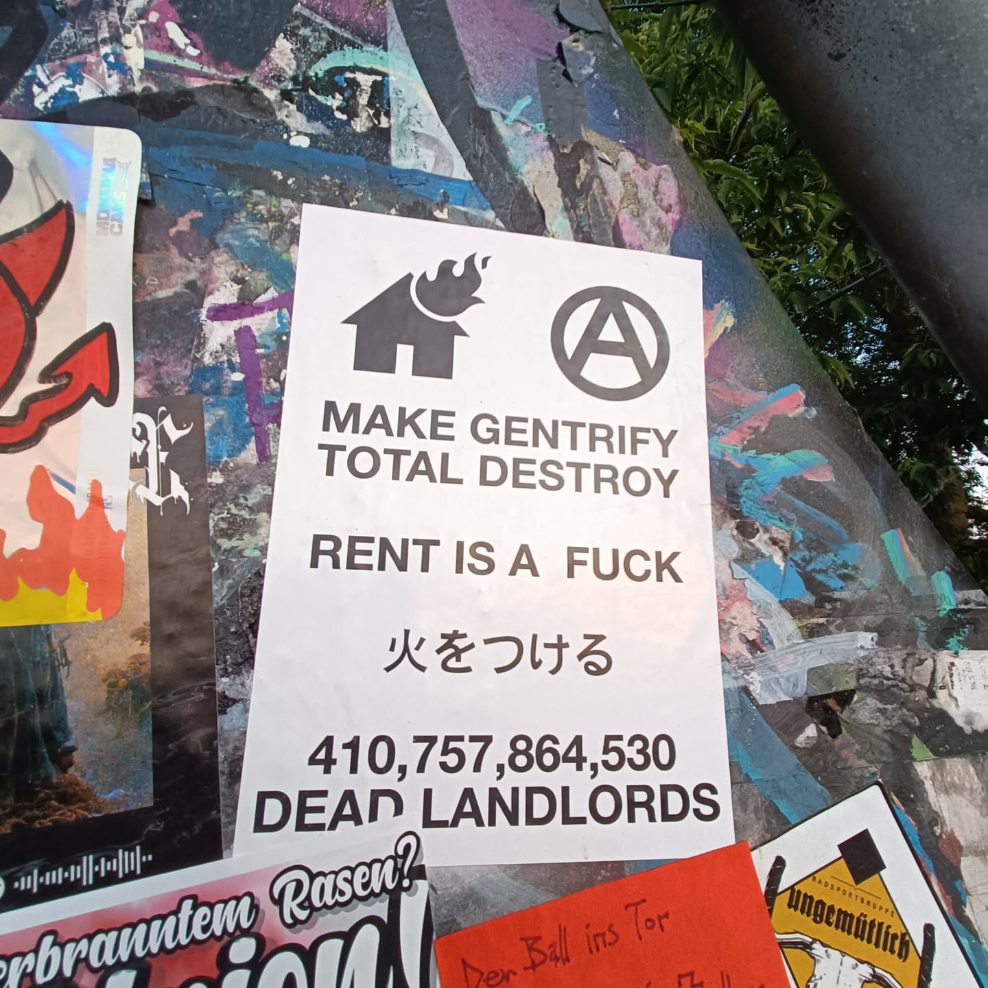 A sticker with an anti-gentrification message. It includes a house with flames, an anarchy symbol, and a large number suggesting a count of landlords.  The text also includes Japanese characters that translate to "set fire".