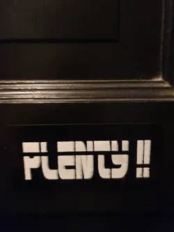 A black and white sticker with the word "Plenty!" in a bold, stylized font. The sticker is affixed to a dark-colored surface.