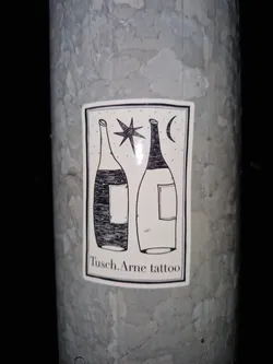 A sticker with a minimalist design featuring two bottles, a star, and a crescent moon. The text "Tusch.Arne tattoo" is visible at the bottom.