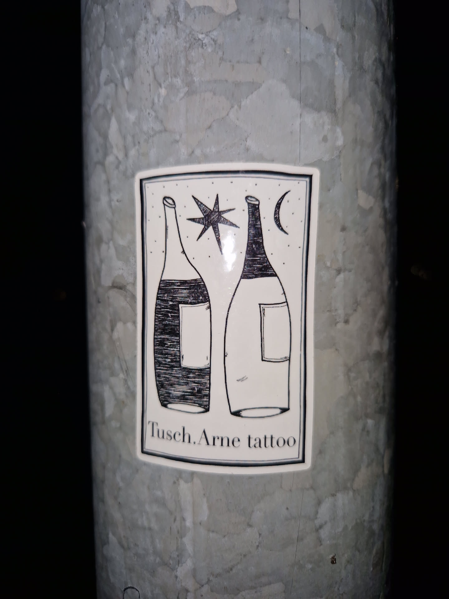 A sticker with a minimalist design featuring two bottles, a star, and a crescent moon. The text "Tusch.Arne tattoo" is visible at the bottom.
