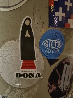 Street sticker A sticker featuring a minimalist illustration of a person in a hijab standing on a red carpet. The text below reads "Restaurante Dona".