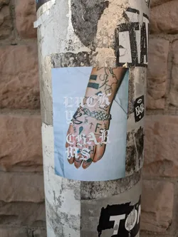 A sticker featuring a close-up of a tattooed hand with the words "LUCK CHARMS" written in a stylized font. The image has a light blue background.