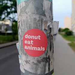 A red circle sticker on a pole with the text "donut eat animals" in white.