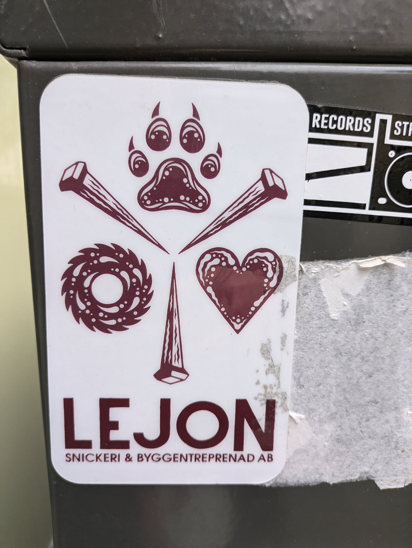 A maroon and white sticker with a paw print in the center, surrounded by nails, a circular saw blade, and a heart. The text 'LEJON Snickeri & Byggentreprenad AB' is written below the design.