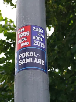 A sticker featuring years of wins (1955, 1959, 1964, 1966, 2002, 2003, 2005, 2019) and the text 'Pokal-Samlare', likely referring to a trophy collector or a team's winning history. The design uses a color-blocked layout with red and blue sections.