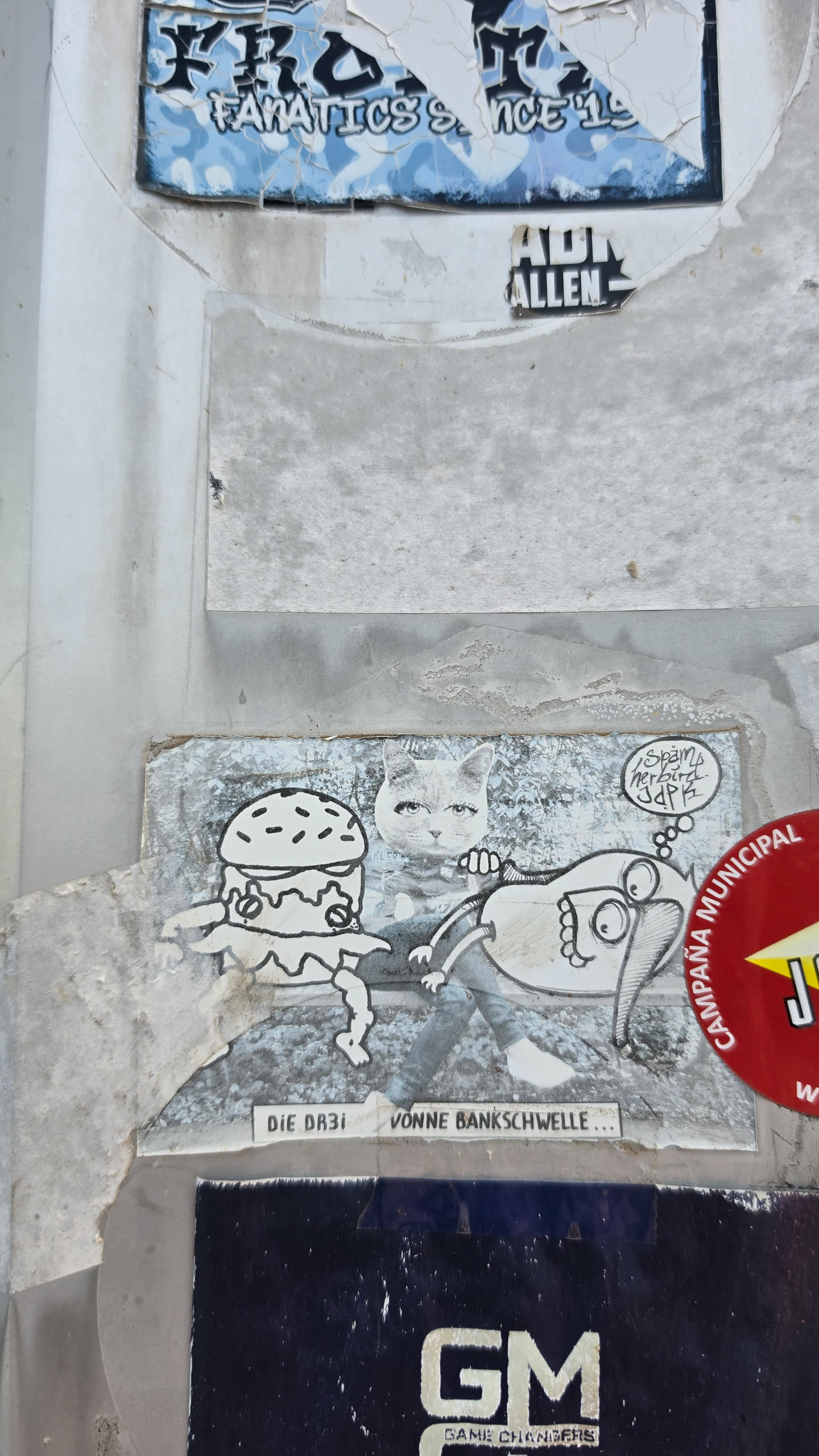 A rectangular, weathered paper sticker featuring a surreal monochromatic collage. In the center sits a figure with a human body in jeans and a realistic cat head with human-like makeup. To the left is an illustrated anthropomorphic burger with spindly legs and arms. To the right is a cartoon creature with large googly eyes, a prominent nose or trunk, and small limbs, with a thought bubble above it containing graffiti-style text. Below the characters, a caption banner reads 'DIE DR3i VONNE BANKSCHWELLE...'.