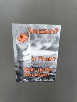 A sticker expressing opposition to Amazon's presence in the Fhain neighborhood.  It depicts a building engulfed in flames. The text translates to "Amazon? In Fhain? Not a good neighbor!"