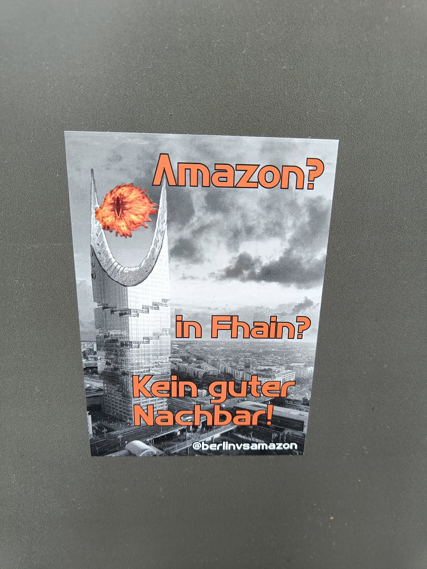 A sticker expressing opposition to Amazon's presence in the Fhain neighborhood.  It depicts a building engulfed in flames. The text translates to "Amazon? In Fhain? Not a good neighbor!"