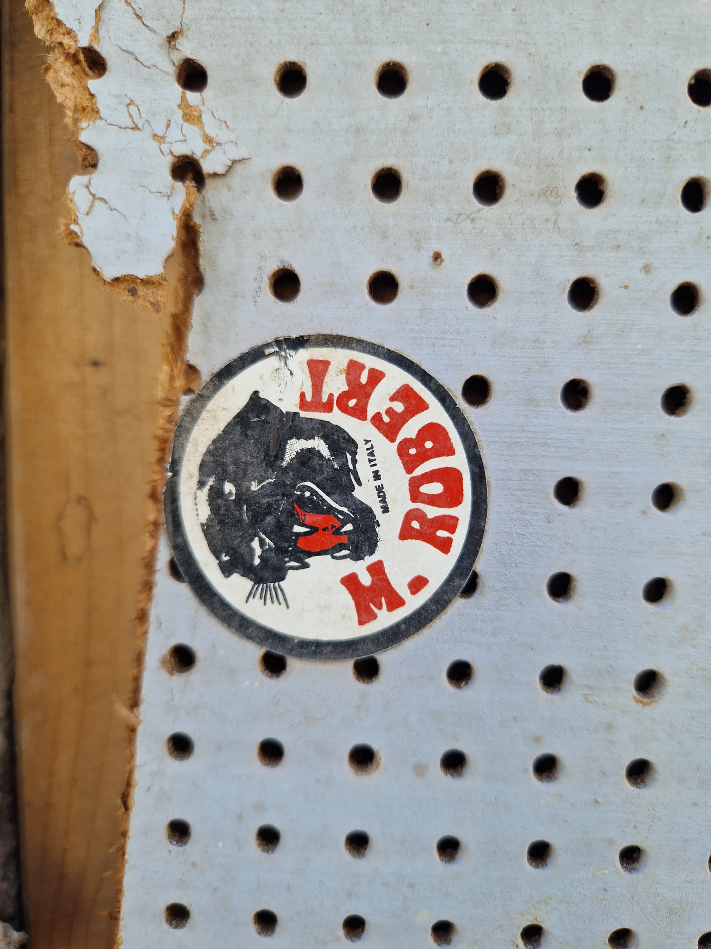 A close-up shot of a round vintage sticker from the brand M. Robert. The sticker features a black panther illustration with red accents and the brand name written around it. The text "Made in Italy" is also visible. The sticker is attached to a pegboard.