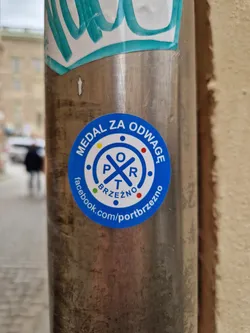 A blue circular sticker with the text "Medal za odwage" (Medal for courage) and a logo. It also contains a Facebook link to Port Brzezno.
