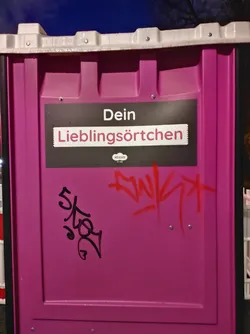 A pink public toilet with a sticker that says "Dein Lieblingsörtchen" (Your favorite place) on it. There is also some graffiti on the sticker.