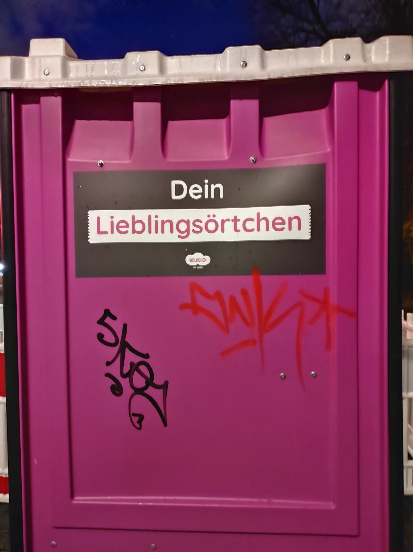 A pink public toilet with a sticker that says "Dein Lieblingsörtchen" (Your favorite place) on it. There is also some graffiti on the sticker.
