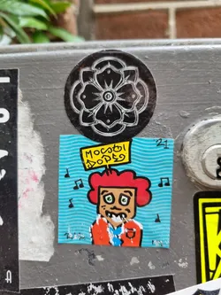 A fun, cartoon-like character with red curly hair is featured on this sticker. The character appears to be holding a sign that says 'Мосгор Дорег', which might be a reference to a location or organization. Musical notes surround the character, adding to the cheerful and musical theme.  A black and white floral sticker is placed on top. 