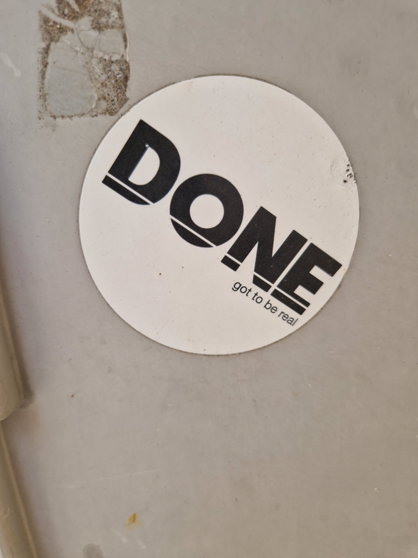 A round white sticker with the word \"DONE\" in bold black letters. Underneath, it says \"got to be real\".