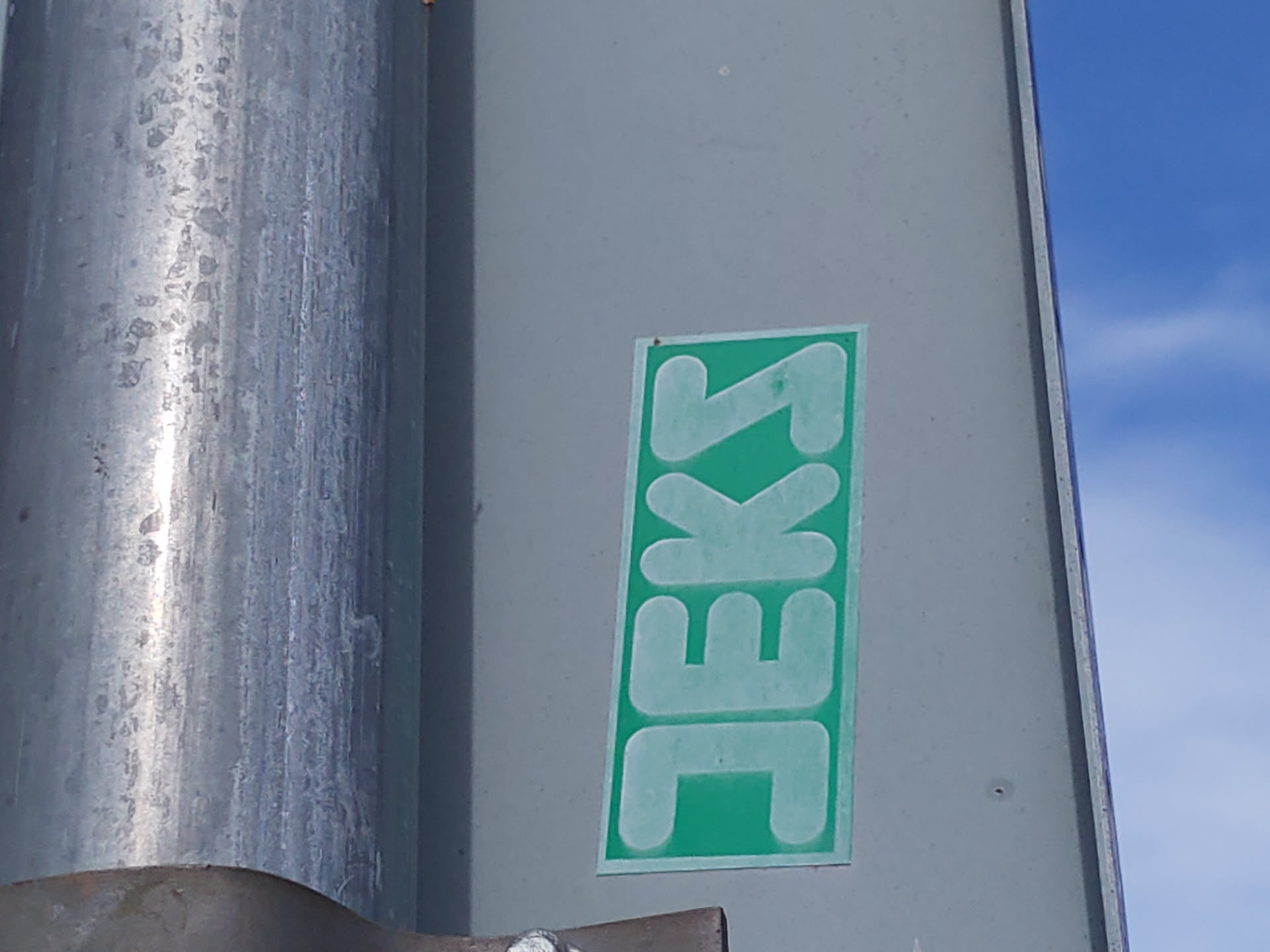 A light teal green sticker with the word Jekks written in a stylized font on a gray metal surface. The sticker is rectangular in shape and appears to be made of vinyl.